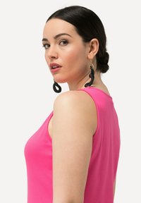 Top senza maniche rosa realizzato in morbido tessuto di cotone, con scollo rotondo. Orecchini neri ondulati completano il look.