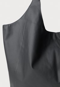 Bolsa de tote negra impermeable con textura suave, gran abertura y un branding sutil. Presenta un detalle de costura mínima para un diseño elegante.