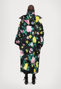Abrigo de plumas largo y negro con un gran estampado floral en rosa y amarillo, que cuenta con capucha, mangas anchas y una silueta cuadrada.