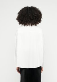 Cămașă albă cu nasturi, cu croială lejeră și detaliu la spate, asortată cu o fustă neagră plisată. Design curat, simplu, fără modele.