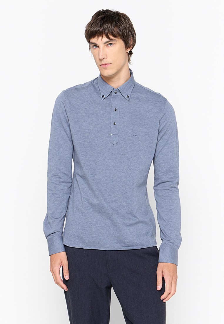 Camisa polo de manga larga en tejido azul claro, con un placket abotonado, cuello con botones oscuros y un patrón texturizado simple.