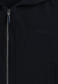 Sweat à zip noir en tissu coton, avec une fermeture éclair à l'avant, des poches latérales et un petit logo brodé sur la poitrine gauche.