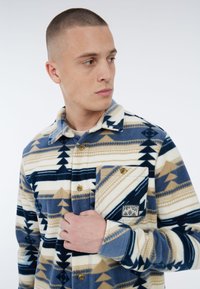 Fleece shirt met een geometrisch patroon in marineblauw, beige en crème. Knopsluiting aan de voorkant, borstzak met logo en kraagontwerp.
