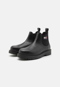 Bottes Chelsea en cuir noir avec des panneaux élastiques sur les côtés, des tirants et une semelle en caoutchouc épaisse dotée d'un motif de relief.