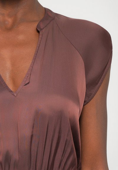 Blouse bordeaux avec un décolleté en V, des manches courtes avec une texture lisse et brillante, et des détails de couture subtils le long des coutures des épaules.