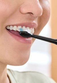 Brosse à dents noire avec des poils souples en utilisation, nettoyant doucement des dents blanches. Gros plan sur la bouche, montrant un alignement dentaire clair et une bonne hygiène.