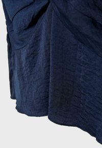 Tissu bleu foncé avec une texture douce et froissée, coutures visibles le long de l'ourlet, tombant naturellement en plis.