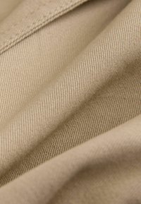 Beige stof med en glat tekstur, der har et diagonalt ribbet vævemønster. Synlige syningsdetaljer langs kanterne og foldene.