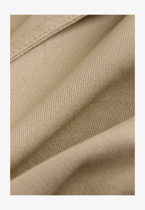 Beżowa tkanina o gładkiej fakturze, z diagonalnym prążkowanym splotem. Widoczne szczegóły przeszyć wzdłuż krawędzi i fałd.