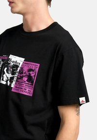 Camiseta de algodón negra con estampados gráficos en rosa y blanco, que representan carteles de conciertos. Manga corta y una etiqueta con el logo en el dobladillo.