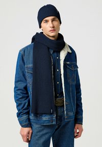 Navy knit hat and scarf, both ribbed texture. Worn with a blue denim jacket and a blue shirt featuring a shearling collar.