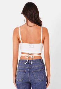 Top corto bianco a costine con spalline regolabili e fiocco sul retro, abbinato a jeans in denim blu a vita alta con tasche posteriori.
