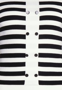 Maglione a righe bianco e nero realizzato in maglia, con una texture a coste, dotato di cinque bottoni neri lungo la linea centrale per la chiusura.
