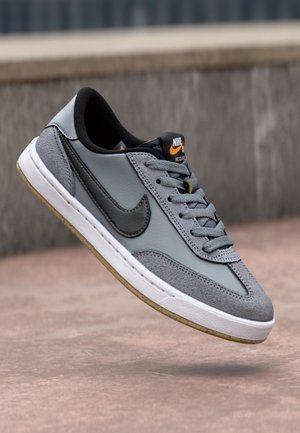 Szaro-czarny but sportowy Nike z białą podeszwą unoszący się nad brukowaną powierzchnią, widok z boku i sznurowadła.