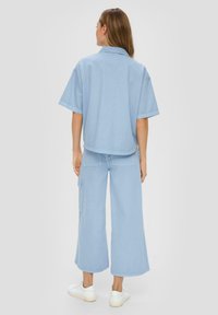 Light blue oversized shirt with short sleeves, paired with matching wide-leg pants. Casual design features two back pockets and a smooth finish.