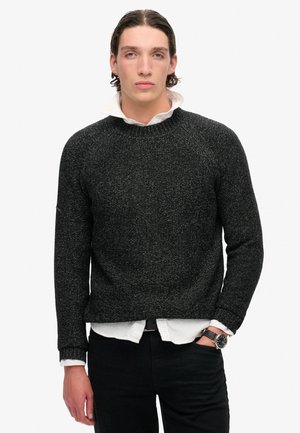 Dunkelgrauer strukturierter Pullover mit rundem Halsausschnitt, Raglanärmeln und gerippten Bündchen, über einem weißen Hemd mit Kragen getragen.