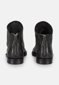 Botas negras hasta el tobillo con cuero perforado, cierre de cremallera en la parte posterior y suelas de goma planas. Textura suave con un diseño aerodinámico.