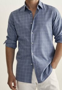 Chemise à carreaux bleus à boutons, en tissu léger, avec un col classique et des manches retroussées, boutonnée sur le devant.