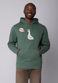 Groene hoodie met een voorzak, met een cartoonzeemeeuw ontwerp en de tekst "MOIN!" in een spraakwolk. Zacht materiaal, relaxte pasvorm.