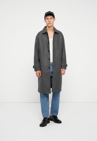 Grijze wollen overjas met een rechte snit, grote knopen en opgerolde manchetten, gedragen over een wit shirt en blauwe spijkerbroeken, gecombineerd met zwarte schoenen.