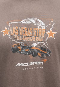 Καφέ βαμβακερό t-shirt με γραφικό αυτοκινήτου Formula 1, κείμενο «Las Vegas Strip» σε πορτοκαλί και πε�ρίγραμμα χάρτη με αστέρια.