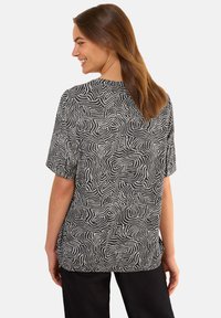 Haut à manches courtes noir et blanc avec un motif en lignes ondulées, coupe décontractée et col rond. Tissu doux au toucher lisse.
