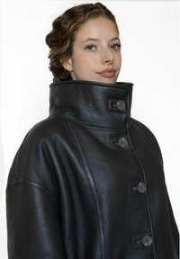 Zwarte leren jas met een hoge kraag, voorzien van een knoopsluiting en brede mouwen. Glad oppervlak met een strak, minimalistisch ontwerp.