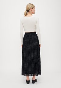 Hvit langermet crop topp kombinert med en svart, prikkete, lang, luftig skjørt. Skjørtet har elastisk midjebånd og mesh-overlag.