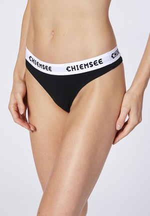 Schwarzer Tanga mit einem weißen Gummibund, auf dem "CHIEMSEE" in schwarzer Schrift steht. Glattes Material mit minimaler Abdeckung und klassischem Design.