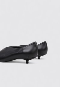 Des chaussures à talons en cuir noir, avec un bout rond et un talon court et épais. La surface est lisse, avec un minimum de détails et une brillance subtile.