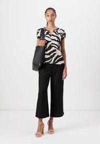 Bluse med sort og beige zebra mønster, matchet med sorte vide bukser og pink strop sandaler. Modellen holder en sort taske.