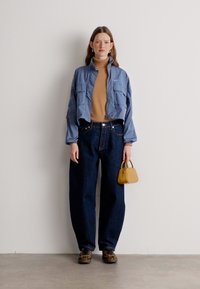 Chaqueta corta azul claro, suéter de cuello alto color arena, pantalones vaqueros anchos oscuros, zapatos de leopardo, bolso pequeño amarillo. Texturas suaves, diseño casual.