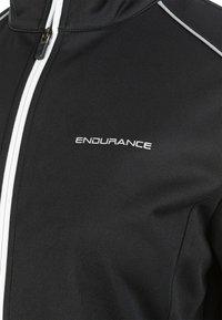 Schwarze Jacke mit hohem Kragen, ausgestattet mit weißen Reißverschluss- und Nähakzenten. "ENDURANCE"-Logo in weiß auf der Vorderseite. Glatter, dehnbarer Stoff.