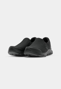 Black slip-on shoes featuring a mesh upper, rubber sole, and minimalistic design. The texture is smooth with no visible patterns or accents.