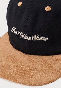 Cappello nero con visiera in camoscio beige. Presenta il testo ricamato "Non Sprecare la Cultura" in bianco, e cuciture marroni sulla visiera.