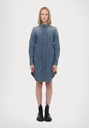 Denim shirt dress, light blue, long sleeves, button-up front, pointed collar, knee-length with high-low hem, featuring a small logo on chest.