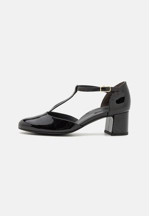 Talons T-strap en cuir verni noir avec un talon carré, un bout rond et un détail de boucle à la cheville. Surface lisse et brillante ; design minimaliste.
