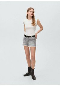 White ribbed top with frill sleeves, paired with light gray denim shorts featuring a raw hem. Black belt with circular buckle and black boots.
