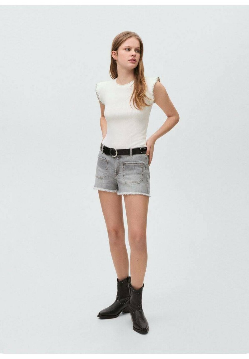 White ribbed top with frill sleeves, paired with light gray denim shorts featuring a raw hem. Black belt with circular buckle and black boots.