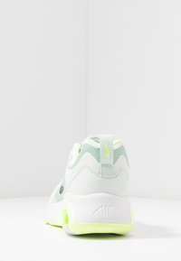 Zapatilla Nike con una combinación de colores blanco y verde claro, materiales de malla y cuero, forma redondeada, suela acolchada y un logotipo prominente.