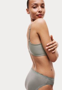 Svetle šedý prádlo, které obsahuje braletku s nastavitelnými ramínky a krajkovým lemem, doplněné o odpovídající kalhotky s krajkovými akcenty.