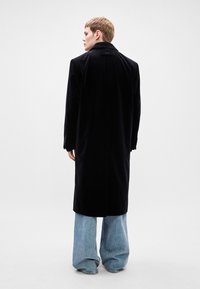 Μαύρο βελούδινο παλτό με κομψή εφαρμογή, αιχμηρές παγιέτες και κλείσιμο με ένα κουμπί, συνδυασμένο με χαλαρά μπλε τζιν.