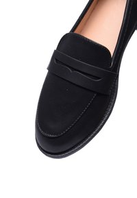 Mocassino in pelle nera con design piatto, punta tondeggiante e cintura decorativa davanti. Texture liscia con suola in gomma.