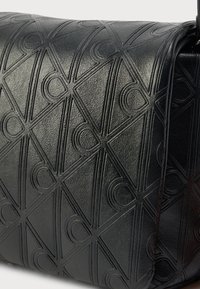 Fekete bőrből készült kézitáska dombornyomott geometriai mintával. Texturált felülettel és strukturált formával rendelkezik, modern dizájnt mutatva.