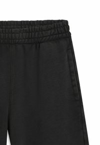 Pantalon de jogging noir avec une taille élastique, doté de poches latérales et d'une texture lisse, conçu pour le confort et la liberté de mouvement.