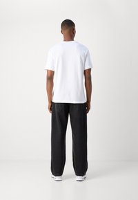 Weißes T-Shirt mit kurzen Ärmeln, kombiniert mit locker sitzenden schwarzen Jeans, die ein schickes Design und eine glatte Baumwolltextur aufweisen. Weiße Sneaker runden den Look ab.