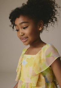 Robe à imprimé floral présentant des couleurs pastel de jaune et de vert, avec des manches volantes et un décolleté carré, fabriquée en tissu léger.