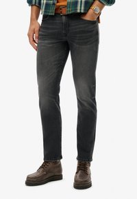 Jeans de mezclilla gris con un ligero estiramiento, que presentan un corte recto clásico, un desvanecimiento mínimo y costuras visibles. Botas de cuero marrón completan el look.