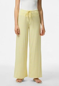 Geel gestreepte wijdvallende broek met een taillekoord, gemaakt van een zachte stof. De strepen zijn een lichtere tint geel tegen de basis kleur.