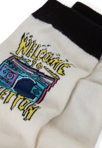 Witte sokken met zwarte boorden, voorzien van een kleurrijk grafisch ontwerp van een vintage cassettespeler en de tekst "WELCOME TO VETTRON." Zachte textuur.